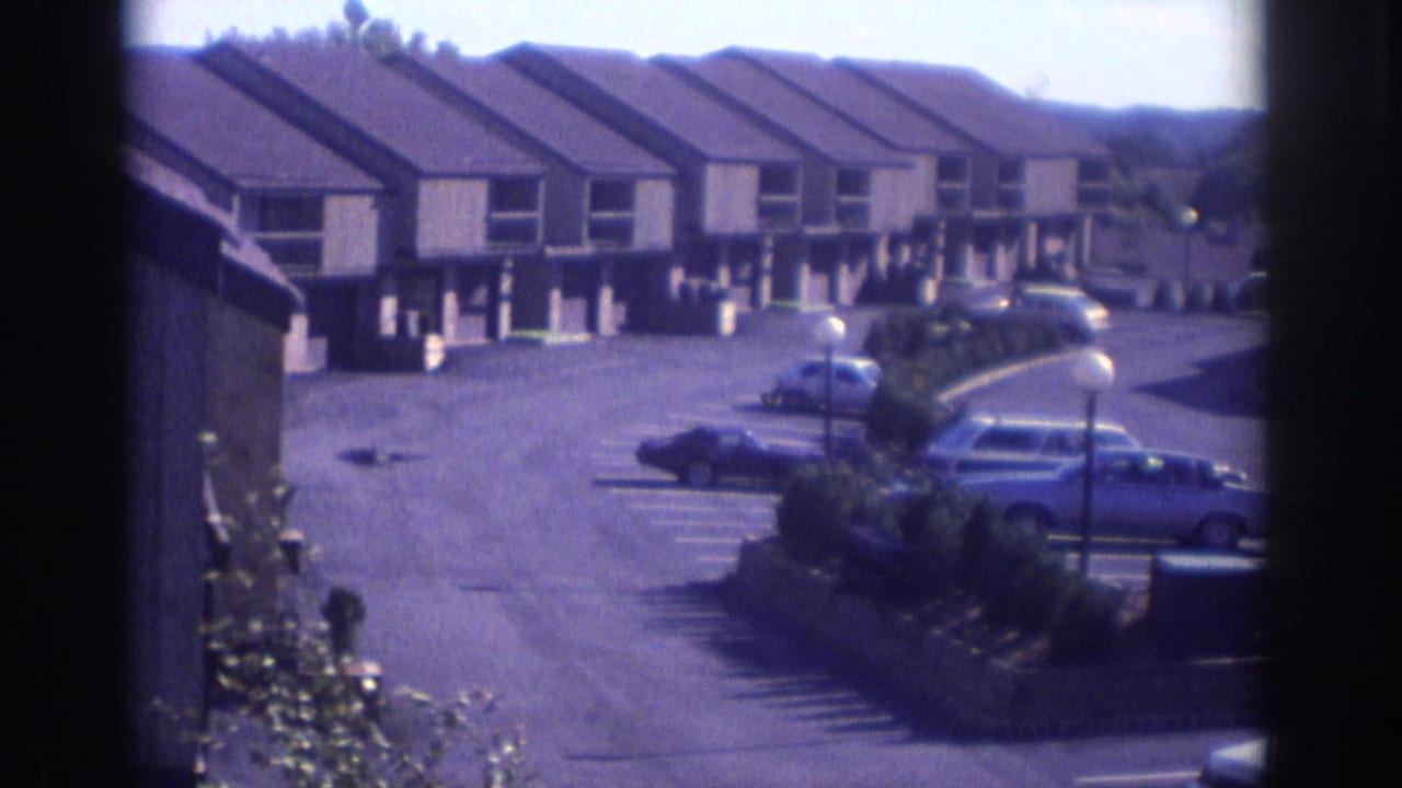 View through a window toward townhouses, parked cars, and a paved residential lot.