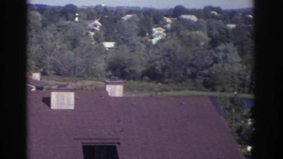 Elevated 1972 Toronto view across a brown roof toward trees, scattered houses, and low hills in the distance.