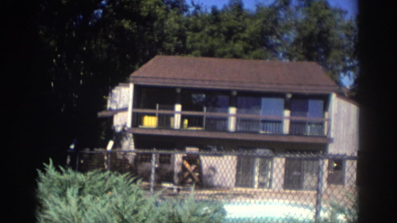 Two-story house and backyard pool seen through a chain-link fence.