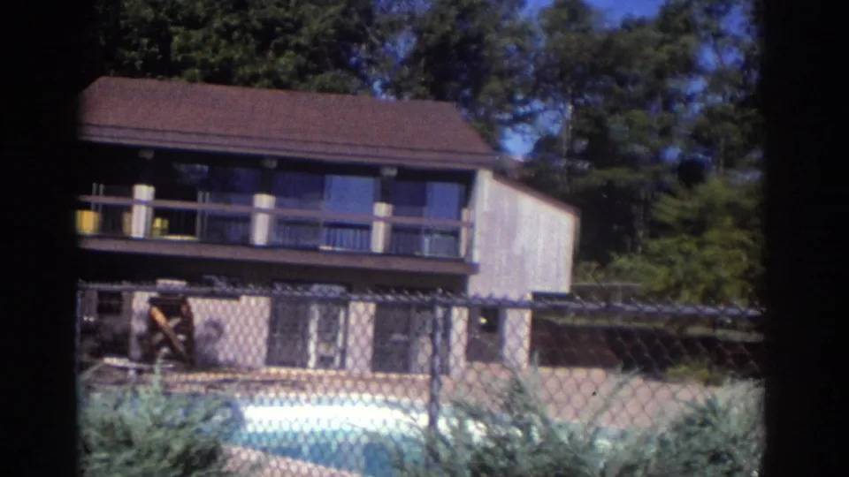 1972 Toronto 8mm frame with a closer handheld view of the two-story house, balcony, fence, shrubs, and pool foreground.