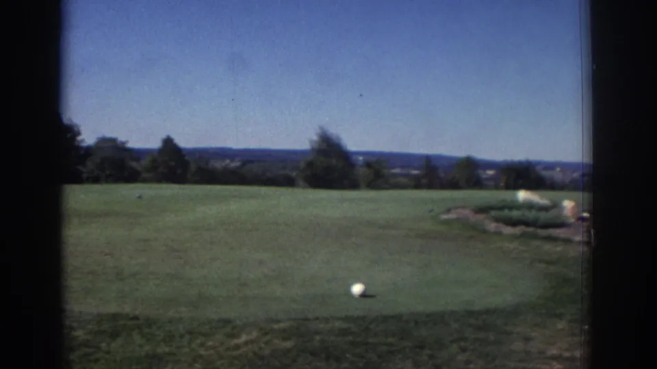 1972 Toronto golf-course view showing a white ball on short grass, with trees and a distant horizon beneath a clear blue sky.