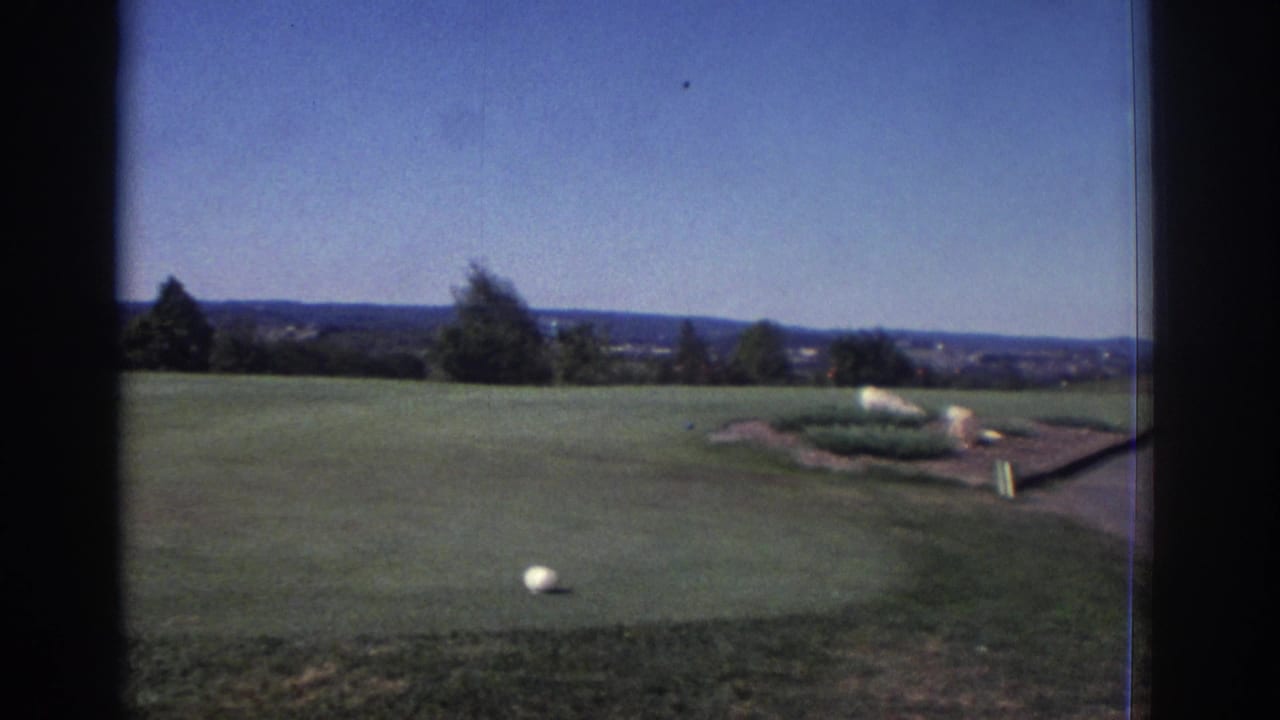 1972 Toronto-area golf course view with a white ball on mown grass, low landscaping, distant hills, and clear daylight sky.