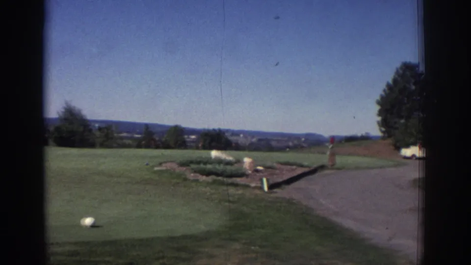 Golf course path and green in 1972 Toronto footage, with a distant person in red near landscaping and open fairway.