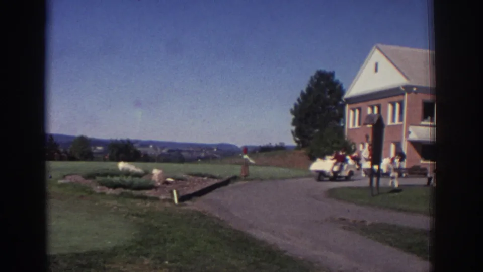 1972 Toronto golf course clubhouse scene with brick building, white trim, people gathered near a golf cart, and parked vintage cars.