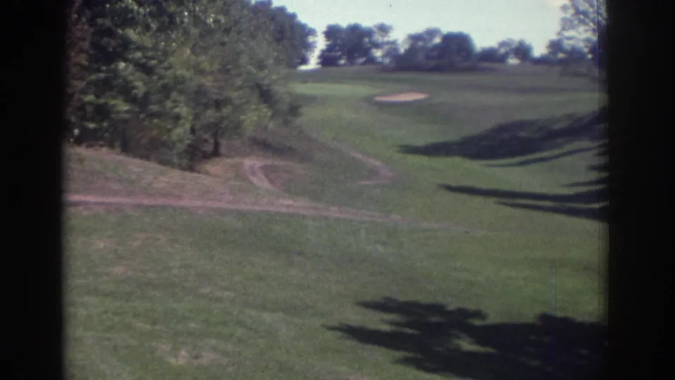 Open 1972 golf course fairway near Toronto, showing trees, a sand trap, a worn track, and long afternoon shadows.