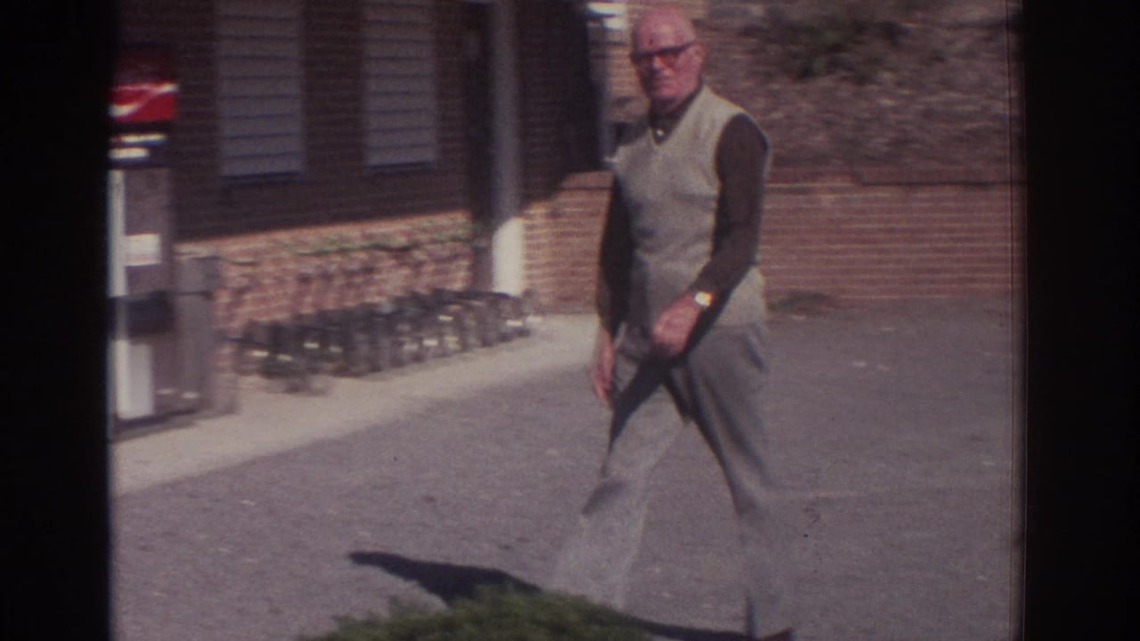 1972 Toronto home-movie frame showing an older man walking past a brick building and visible Coca-Cola vending machine.