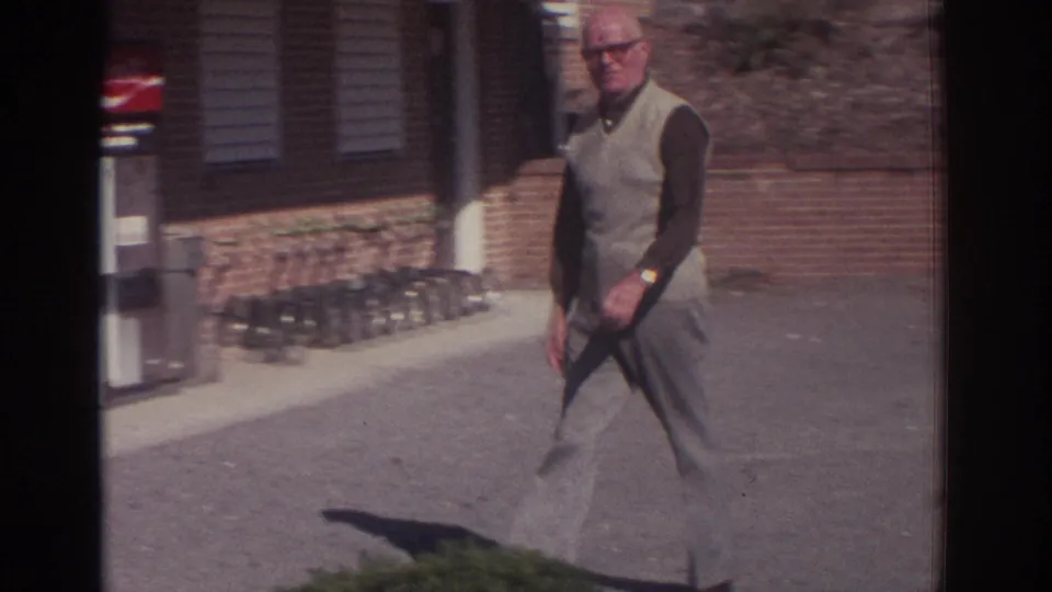1972 Toronto home-movie frame showing an older man walking past a brick building and visible Coca-Cola vending machine.