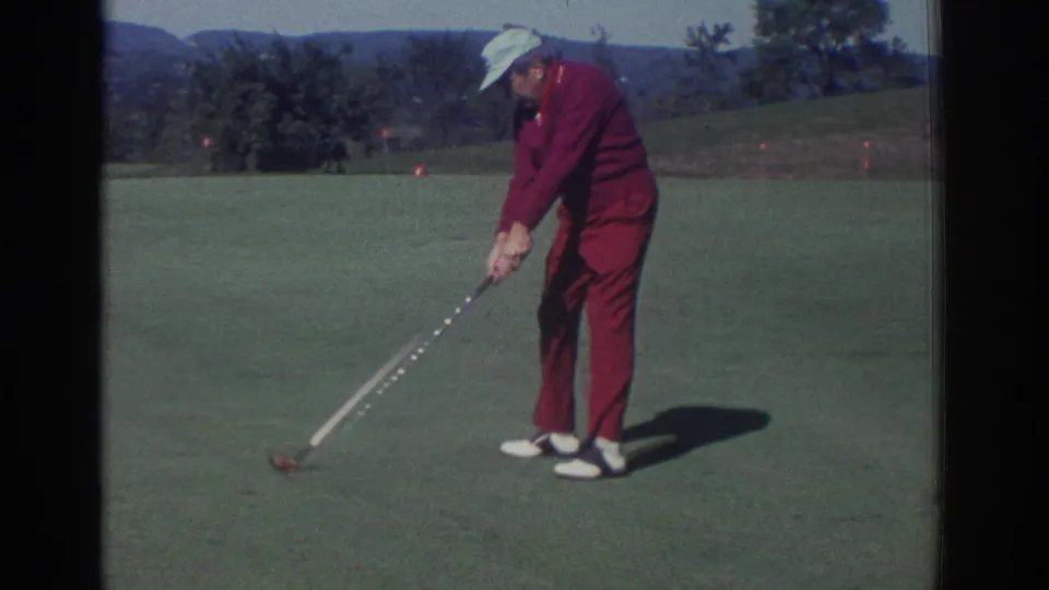 1972 Toronto home-movie frame of a man in a red tracksuit preparing to strike a golf ball on a sunny course.