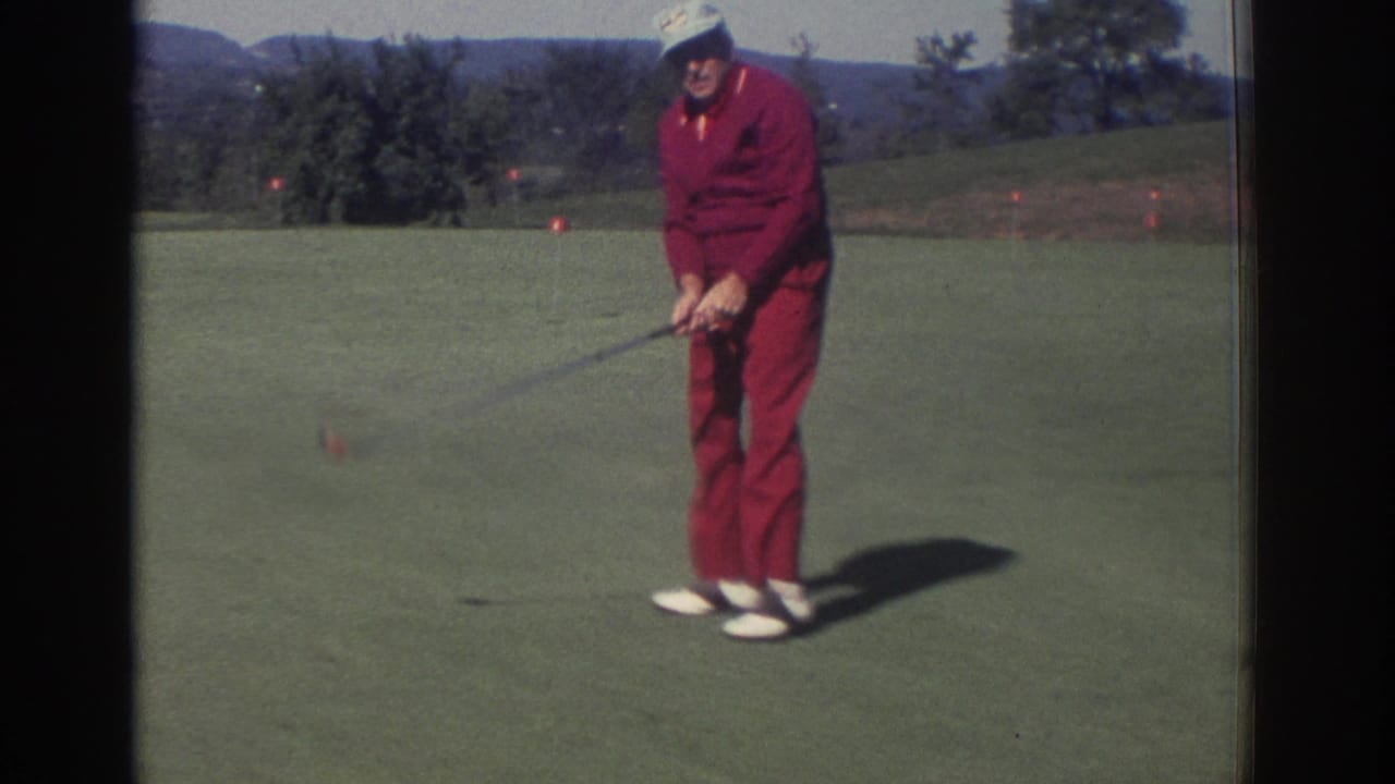 Adult man in a red tracksuit prepares to putt on a golf green.