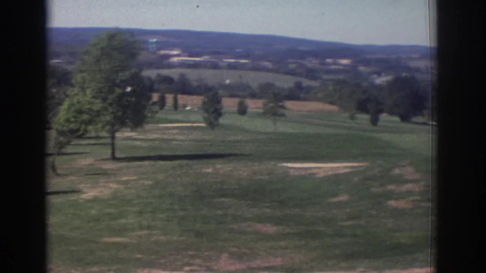 1972 Toronto home-movie view across a golf course, showing fairway grass, scattered trees, bare ground, and distant rolling hills.