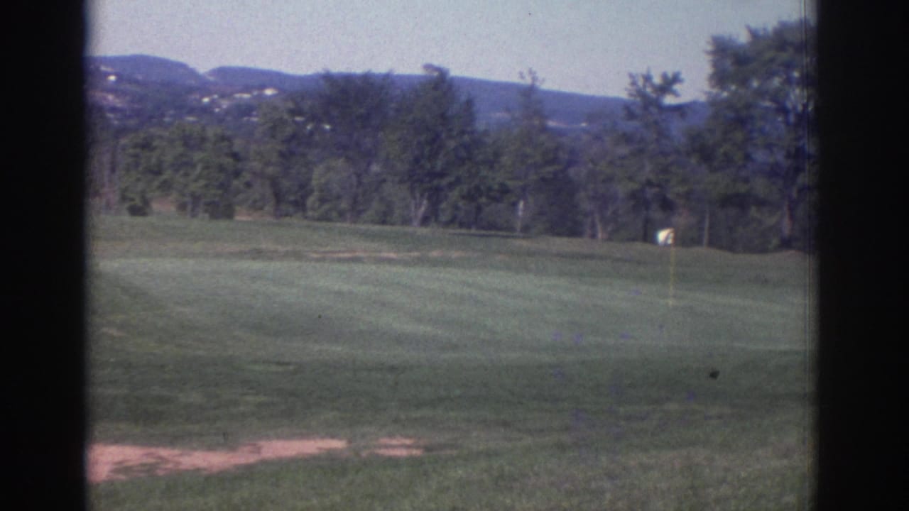 1972 Toronto-area home-movie view of a green golf fairway with trees, distant hills, and a small pale course marker.