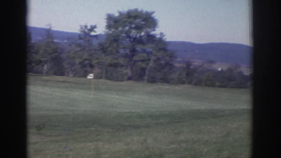 Wide 8mm view of a Toronto golf course, showing manicured grass, trees, distant hills, and a small pale marker.