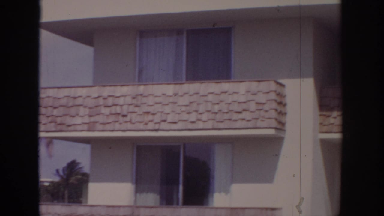 1973 Naples, Florida 8mm frame showing cream apartment balconies, shingled balcony fronts and windows behind dark foreground bars.
