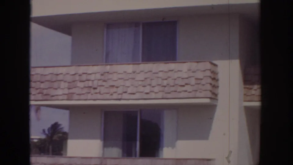 1973 Naples, Florida 8mm frame showing cream apartment balconies, shingled balcony fronts and windows behind dark foreground bars.
