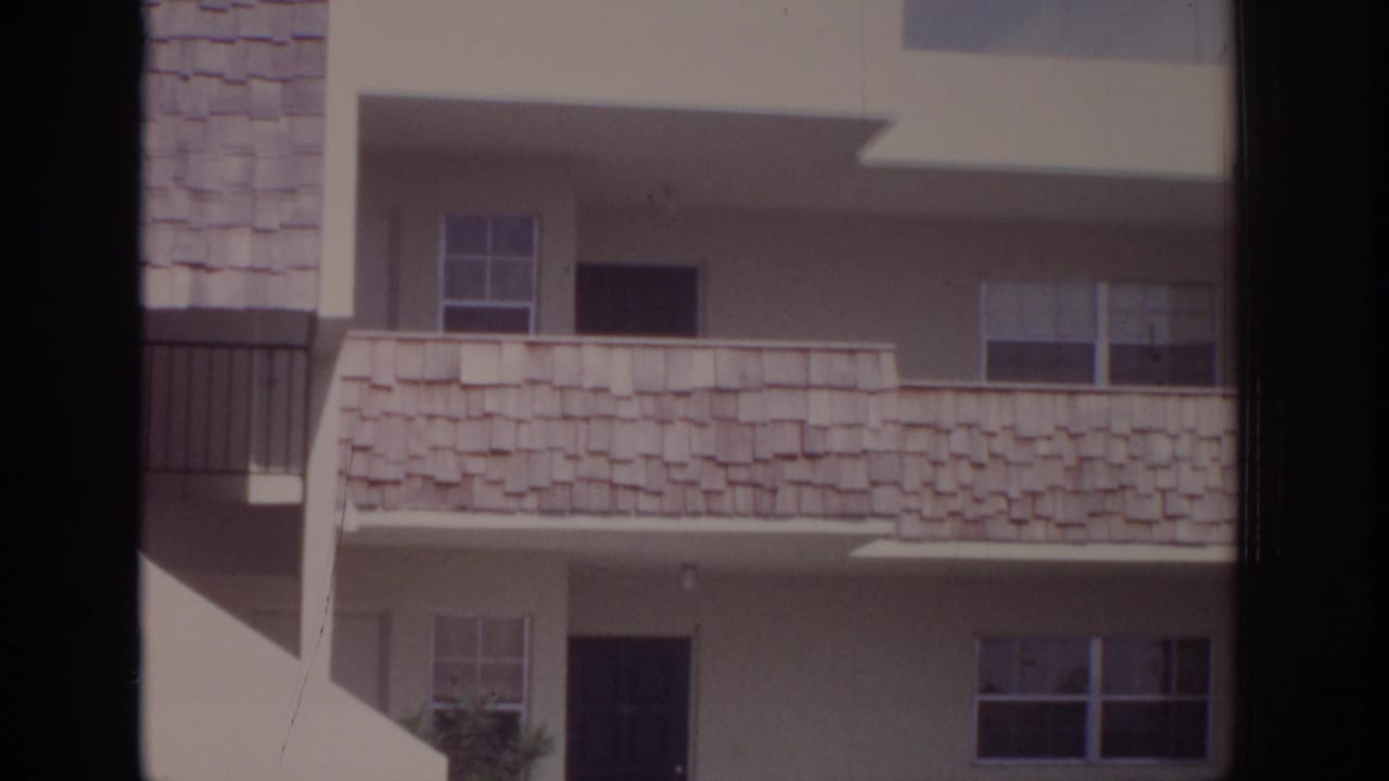 1973 Naples, Florida apartment exterior with white stucco walls, shingled balcony panels, dark doors, windows, and a small landscaped edge.