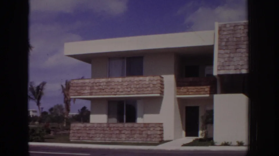 1973 Naples, Florida apartment building seen from across a road, with shingled balcony fronts, white walls, dark doorway, windows, and blue sky.