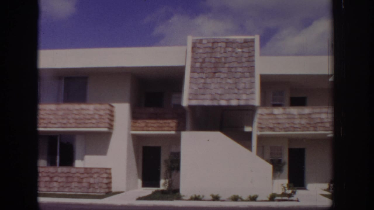 Naples, Florida, 1973 home-movie frame showing a two-story white stucco apartment facade with shingled balcony panels and dark entries.