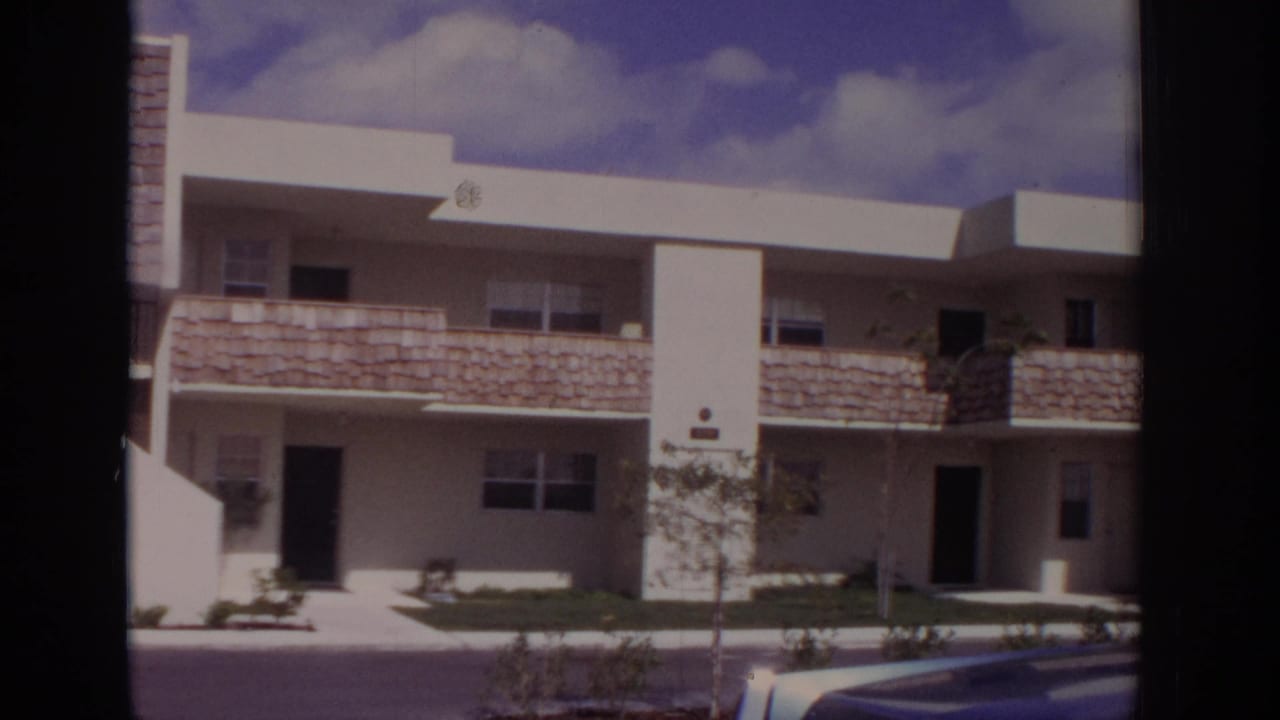 Naples, Florida, 1973 view of a white two-story residential building with flat roofs, stone-textured balcony panels, lawn, and parked car edge.