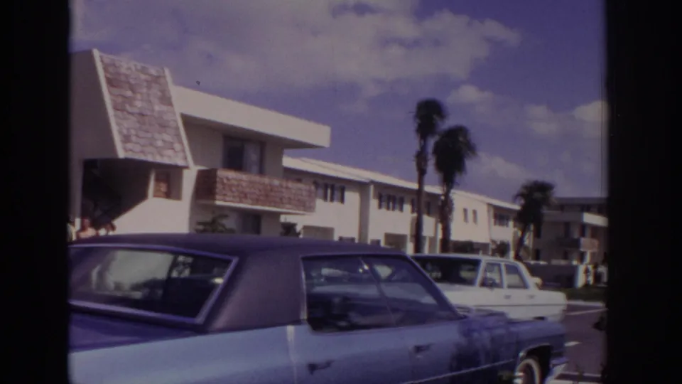 Naples, Florida, 1973 parking-lot view with white apartment-style buildings, palm trees, and large parked American sedans.