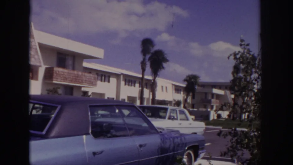 Naples, Florida, 1973 view of a light blue sedan parked near white low-rise residential buildings and palm landscaping.