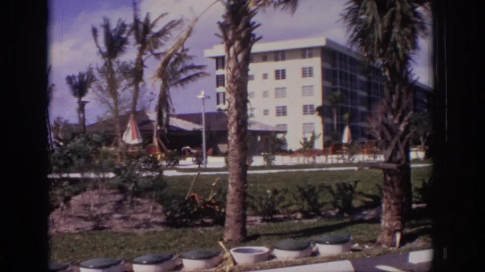 1973 Naples, Florida home-movie frame showing palms, planters, lawn, and a white apartment building in a tropical setting.