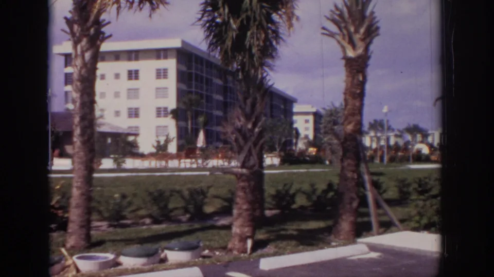 1973 Naples, Florida home-movie view of an apartment exterior with palms, planters, lawn, walkway, and a paved foreground.