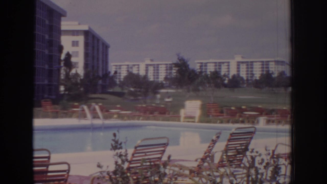 1973 Naples, Florida resort pool area with striped lounge chairs, lawn, and modernist buildings seen through soft 8mm color.