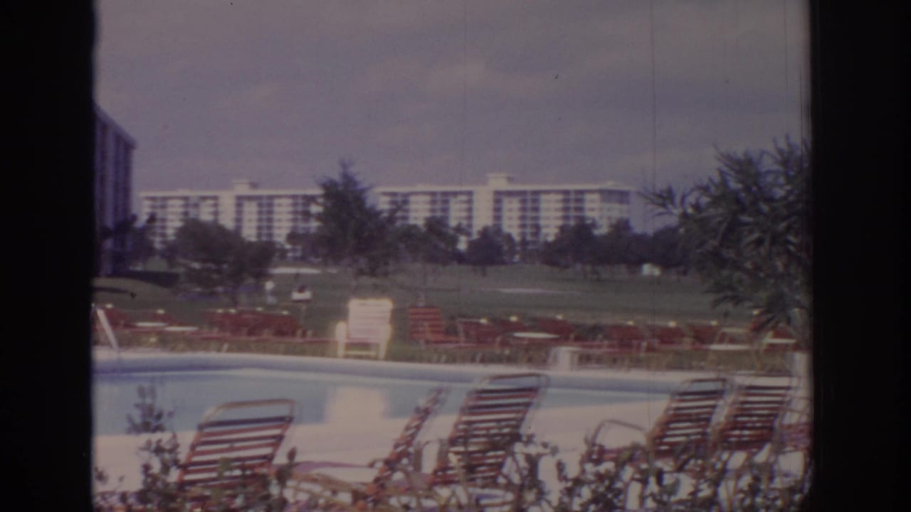 Naples, Florida resort pool scene from 1973, with red-striped loungers, lawn, trees, and distant apartment-style buildings.