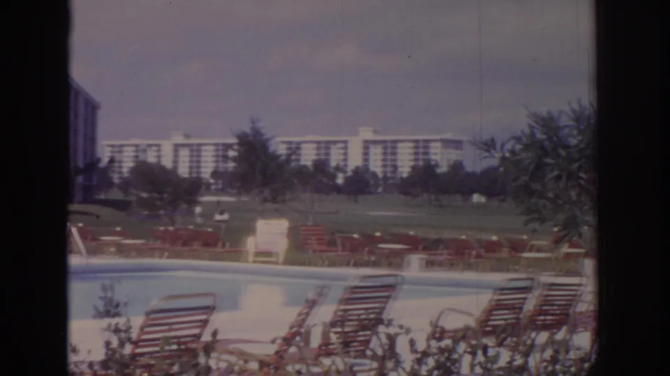Naples, Florida resort pool scene from 1973, with red-striped loungers, lawn, trees, and distant apartment-style buildings.