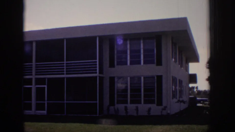1973 Naples, Florida frame showing a two-story apartment building with screened porch panels, broad windows, and a small lawn.