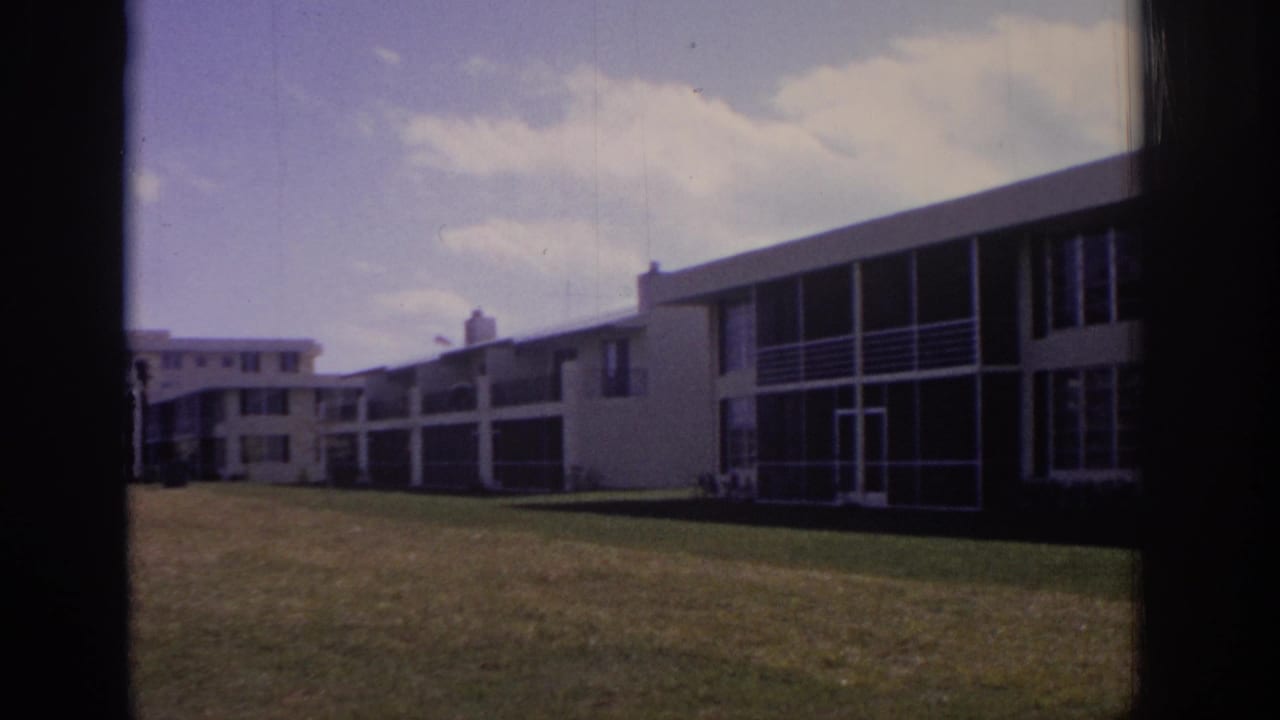 Low-rise residential buildings seen across a lawn with dark film-frame borders.