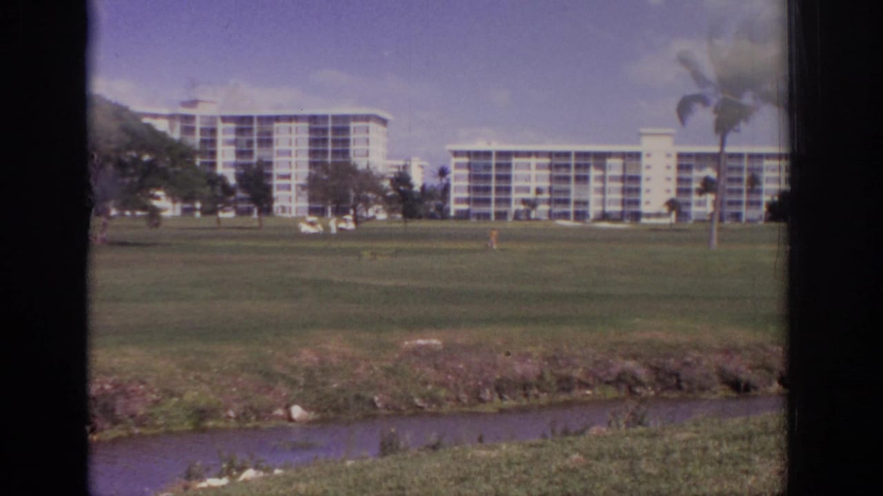 1973 Naples, Florida home-movie view of resort-like buildings beyond a lawn, with palms and a shallow waterway in the foreground.