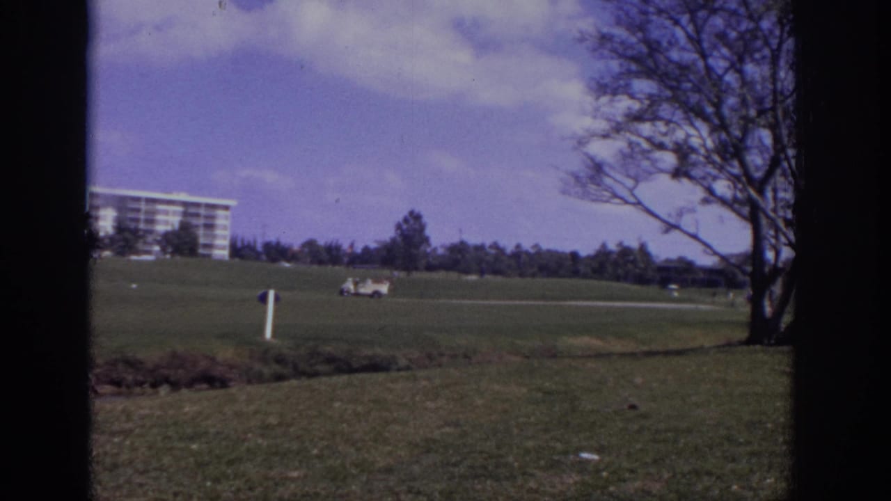 1973 Naples, Florida golf-course view with a distant resort-style building, golf cart, open lawn, and dark 8mm frame edges.