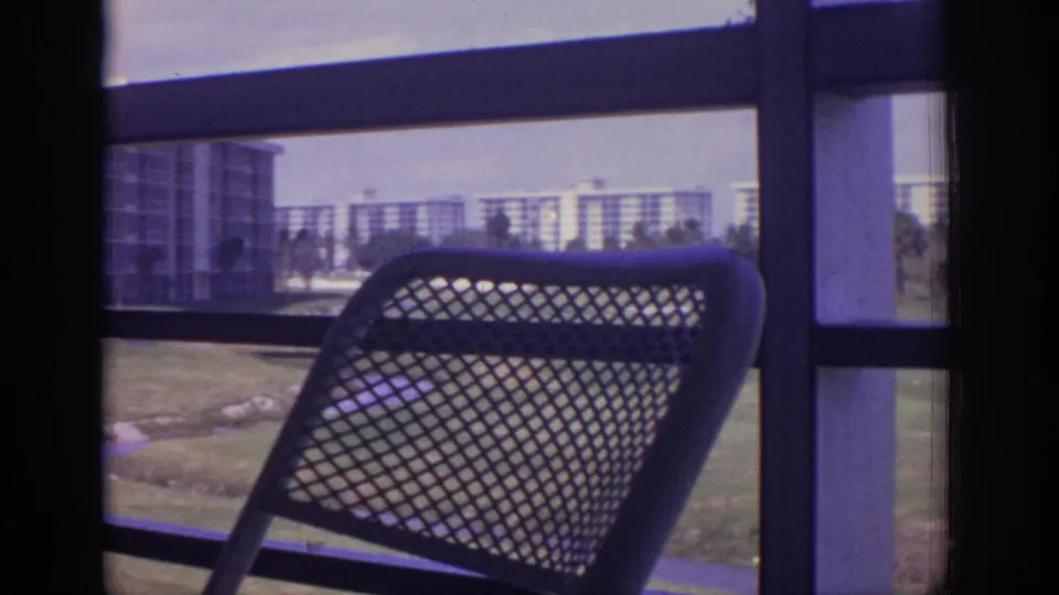 A 1973 Naples patio view shows a mesh chair in front of balcony framing, with lawn, palms, and multi-story buildings beyond.