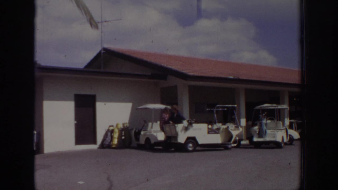 1973 Naples, Florida home-movie frame showing white golf carts, golf bags, and people near a low red-roofed golf course building.