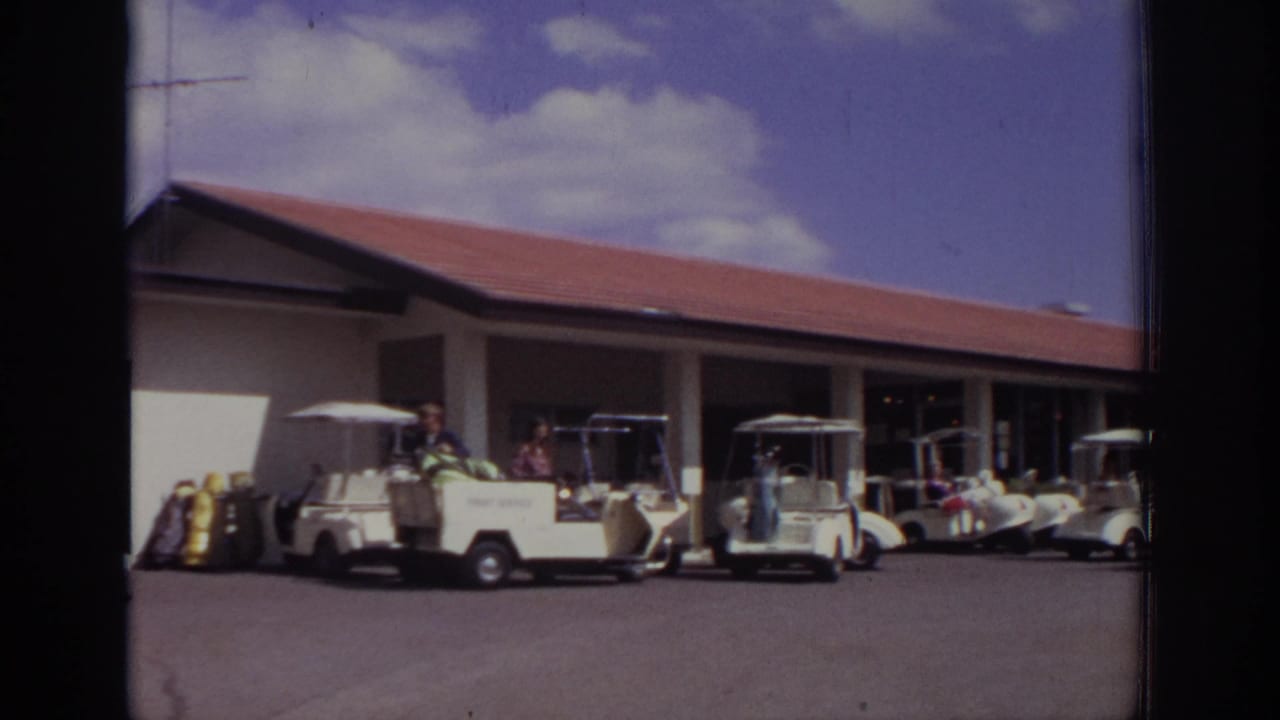 Several white golf carts parked in front of a long red-roofed building.