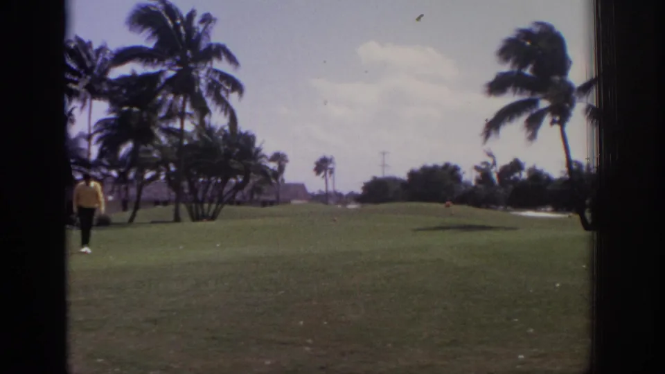 1973 Naples, Florida 8mm view of a windy palm-lined golf course with a golfer in yellow at the left edge of frame.
