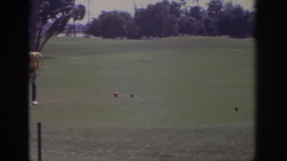 The Naples golf-course view holds on open grass, scattered tee markers or balls, and the partly cropped golfer at the left edge.