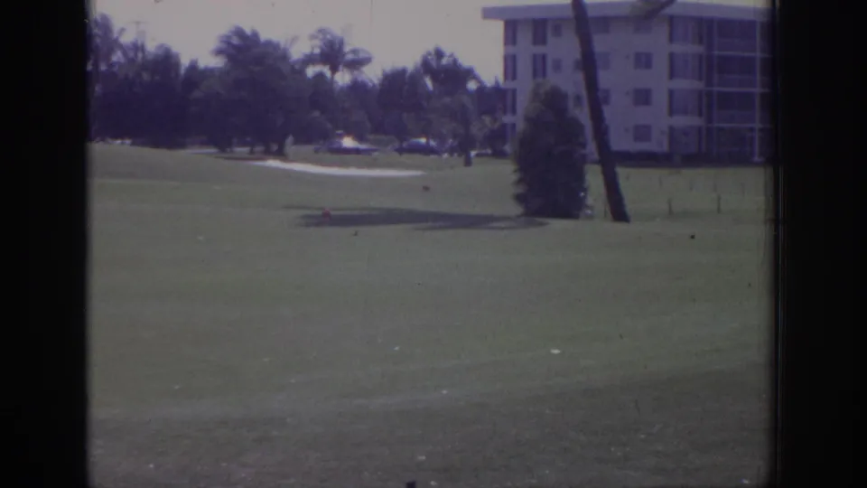 1973 Naples, Florida 8mm frame showing a golf course, bent palm trees, and resort buildings during strong wind.