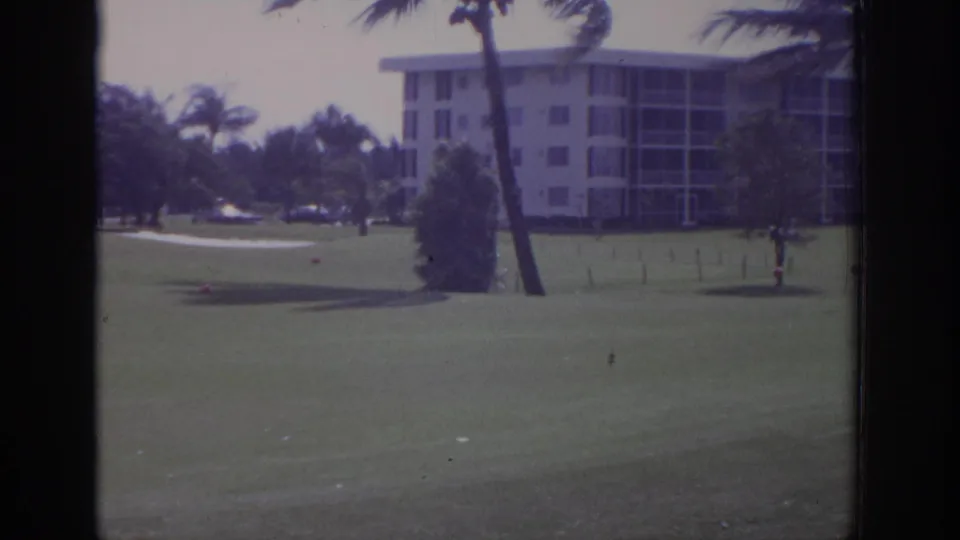 1973 Naples, Florida 8mm frame of a resort golf course with palms leaning in wind and an indistinct person at right.