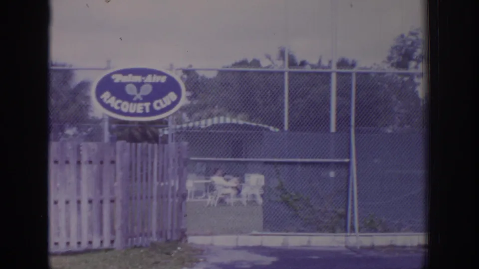 1973 Naples, Florida 8mm frame showing a Palm-Aire Racquet Club sign behind a fence during storm conditions.