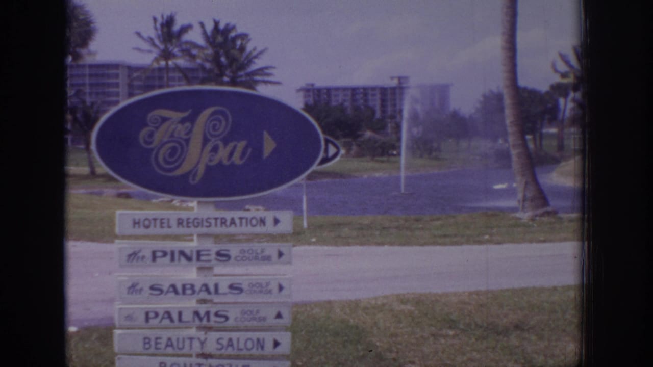 1973 Naples, Florida 8mm frame showing The Spa entrance sign, directional boards, palms, lawn, fountain spray, and distant buildings.
