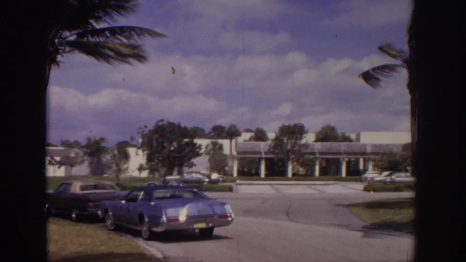 Parked early-1970s cars line a driveway in front of a low modern resort building in Naples, Florida.