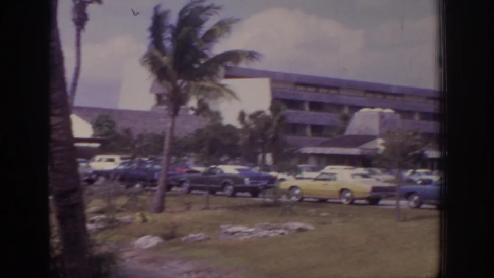 1973 Naples, Florida resort parking area with a larger hotel building, palm trees, grass, and classic cars including a yellow sedan.