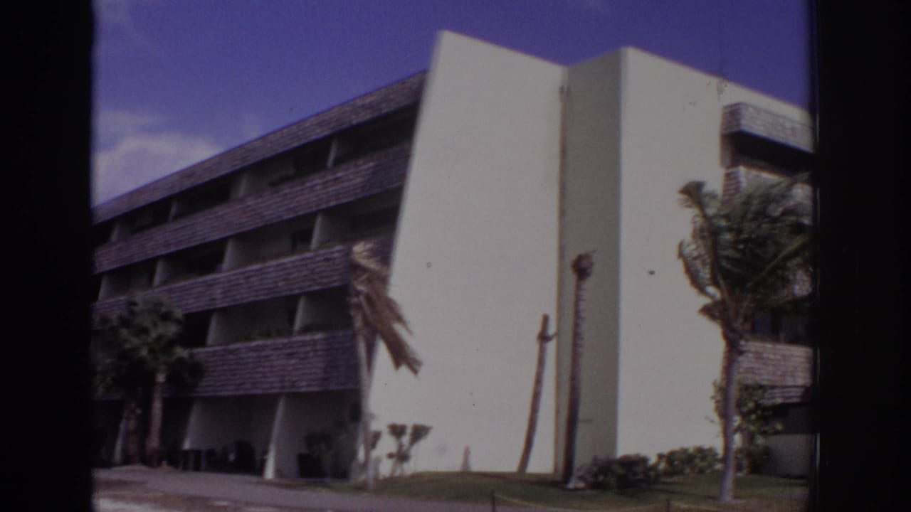1973 Naples, Florida 8mm frame showing a white modernist building, dark balcony bands, lawn, and windblown palms.