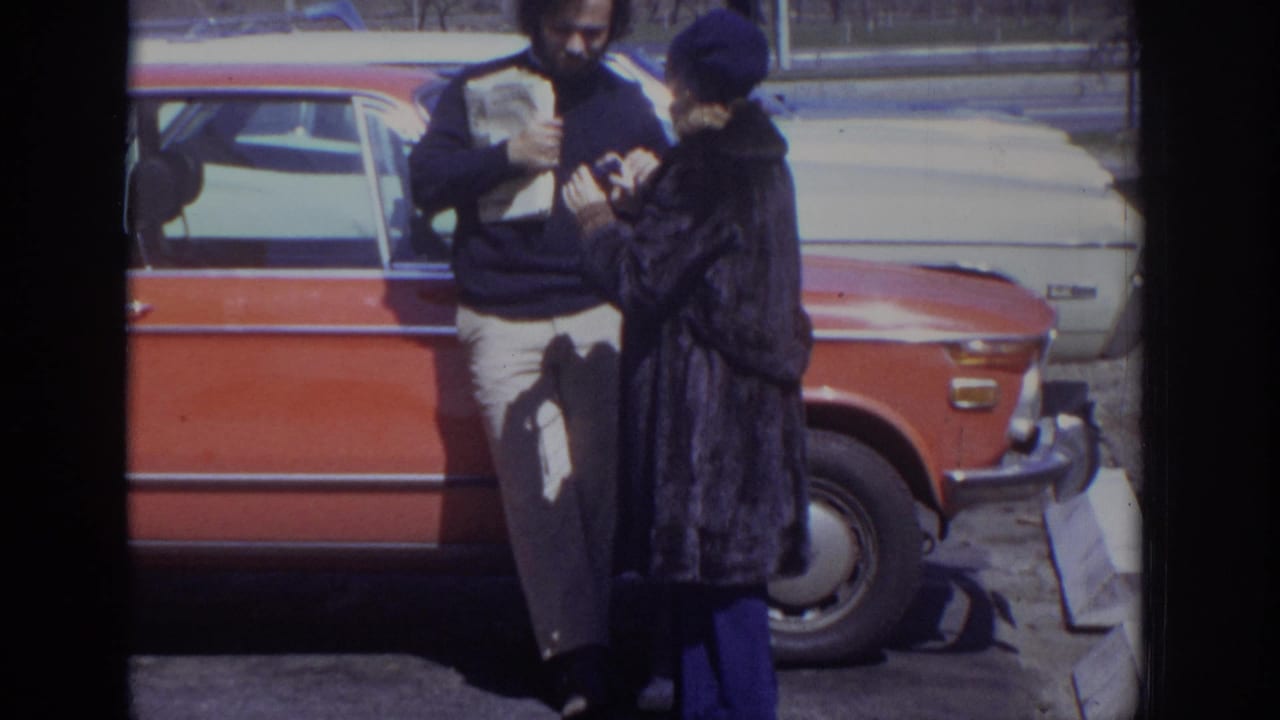 In 1973 Philadelphia home-movie footage, a man and woman stand by a red station wagon and look at something in their hands.