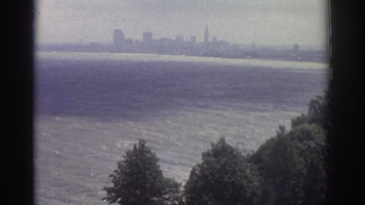 Window-framed view across water toward a hazy skyline with trees below.