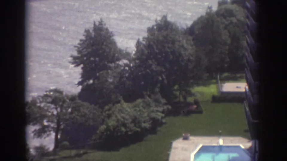 1974 Cleveland 8mm frame looking down from a tall building toward trees, grass, lake water, and the edge of an outdoor pool.
