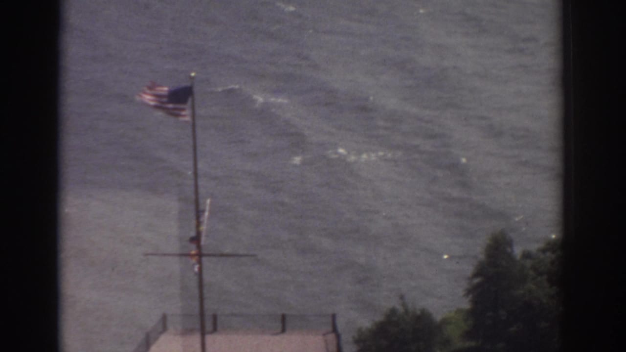 American flag blowing in wind against rippling water.