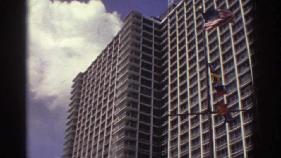 1974 Cleveland view of a tall modern high-rise with grid windows, clouds, and flags along the edge of the frame.